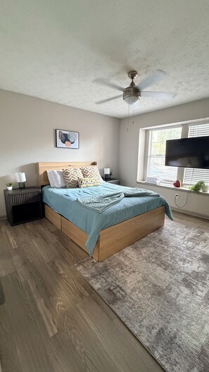 A bedroom with a bed, a ceiling fan, a TV, a window, and a nightstand. - 2BR 4min The Braves Pool, Gym & Private Patio (Smyrna)