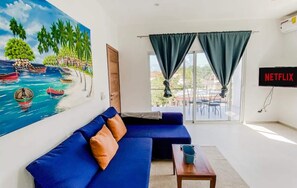 Una sala de estar con un sofá azul, un cuadro de una playa tropical, una mesa con un cubo y un cartel de Netflix.