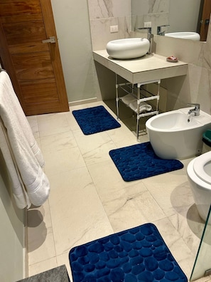 Un bany amb un lavabo blanc, un vàter i un mirall. Hi ha dos estebuts blaus a terra.