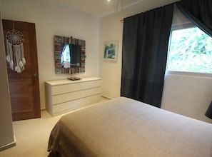Un dormitori amb llit, una petaca, un penjador de somnis, un mirall i una finestra amb cortines.