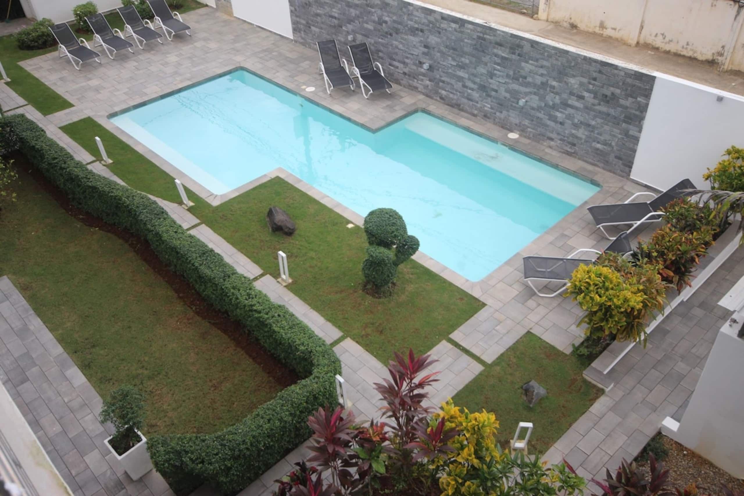 A rectangular outdoor swimming pool with a stone wall and a paved deck area.