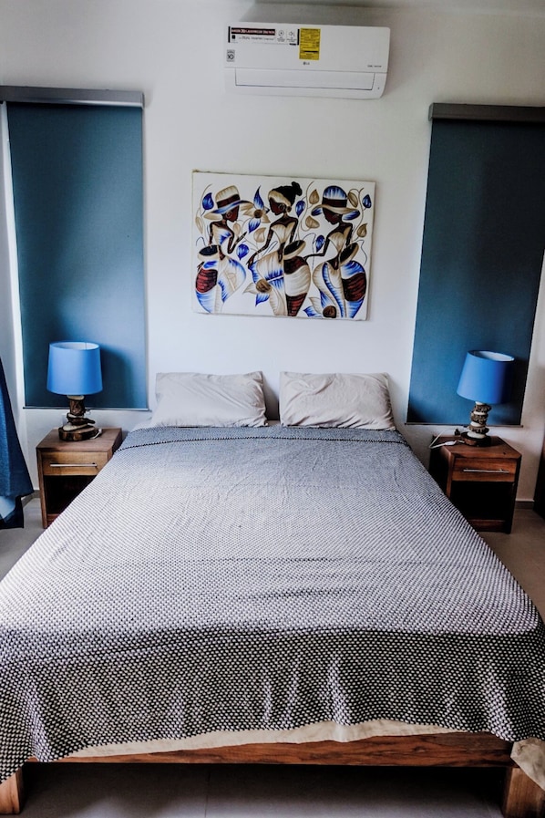 Un dormitorio con una cama, dos mesitas de noche, un aire acondicionado de pared y un cuadro.
