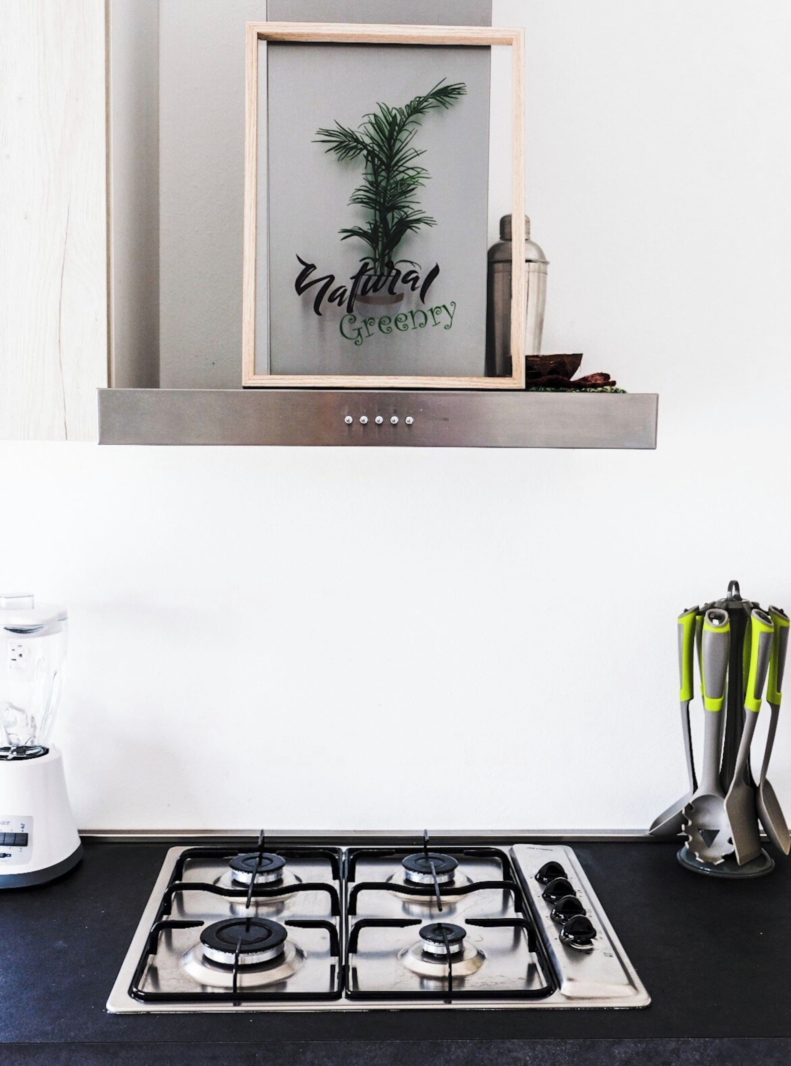 Una cocina con una obra de arte enmarcada en la pared, una estufa a gas y una licuadora en la encimera.