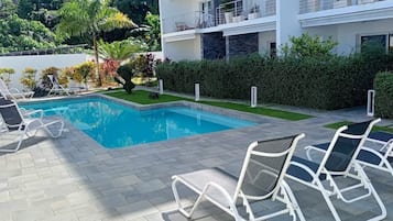 A swimming pool with lounge chairs, a landscaped garden, and a multi-story building in the background.