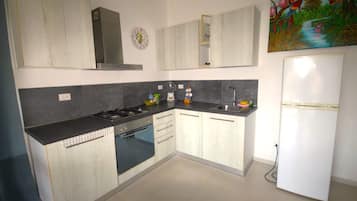 A modern kitchen with a gas stove, oven, and sink. There is a refrigerator and a clock on the wall.