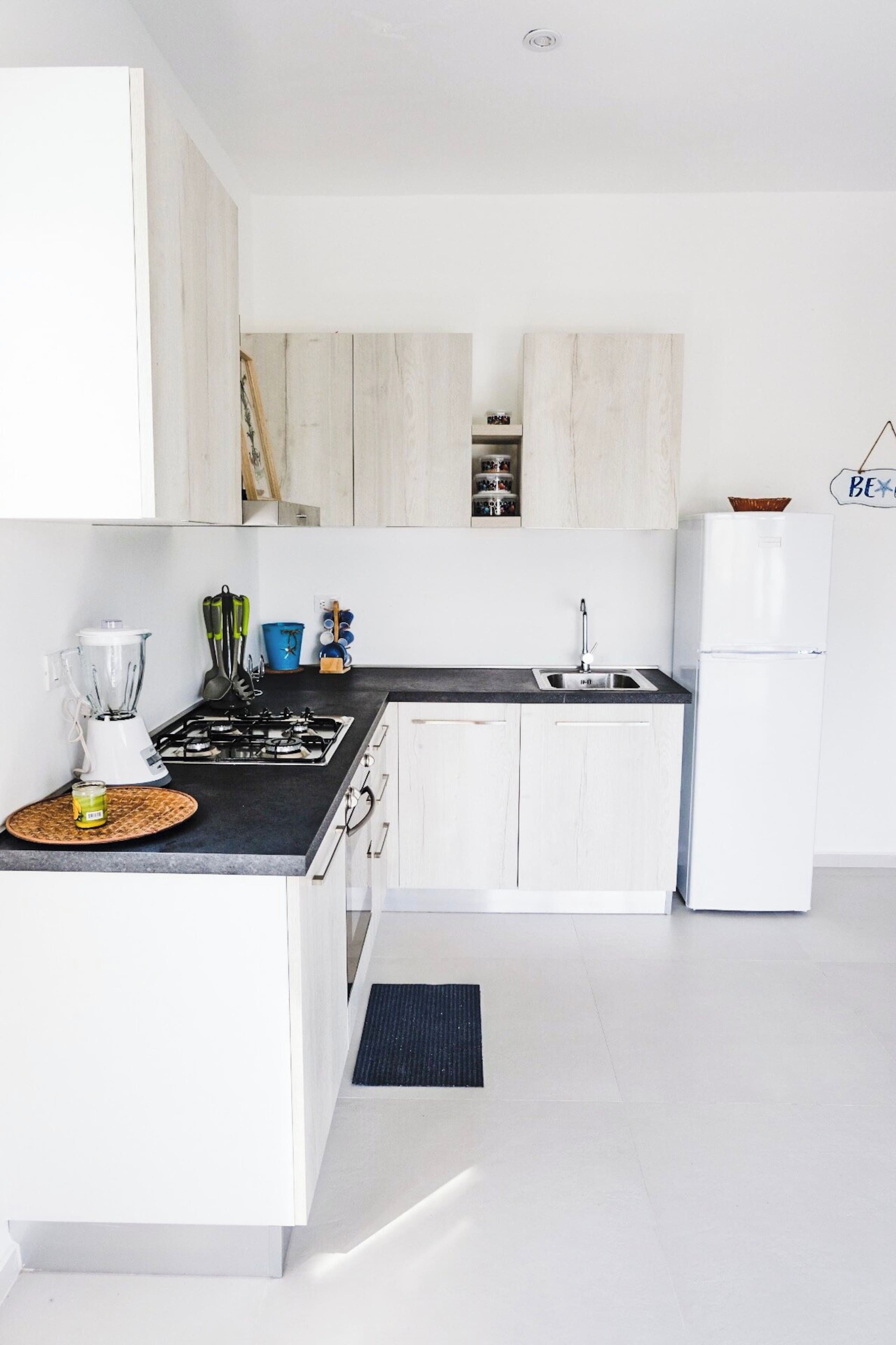 A modern kitchen with white cabinetry, a black countertop, a built-in stove, a sink, and a refrigerator.