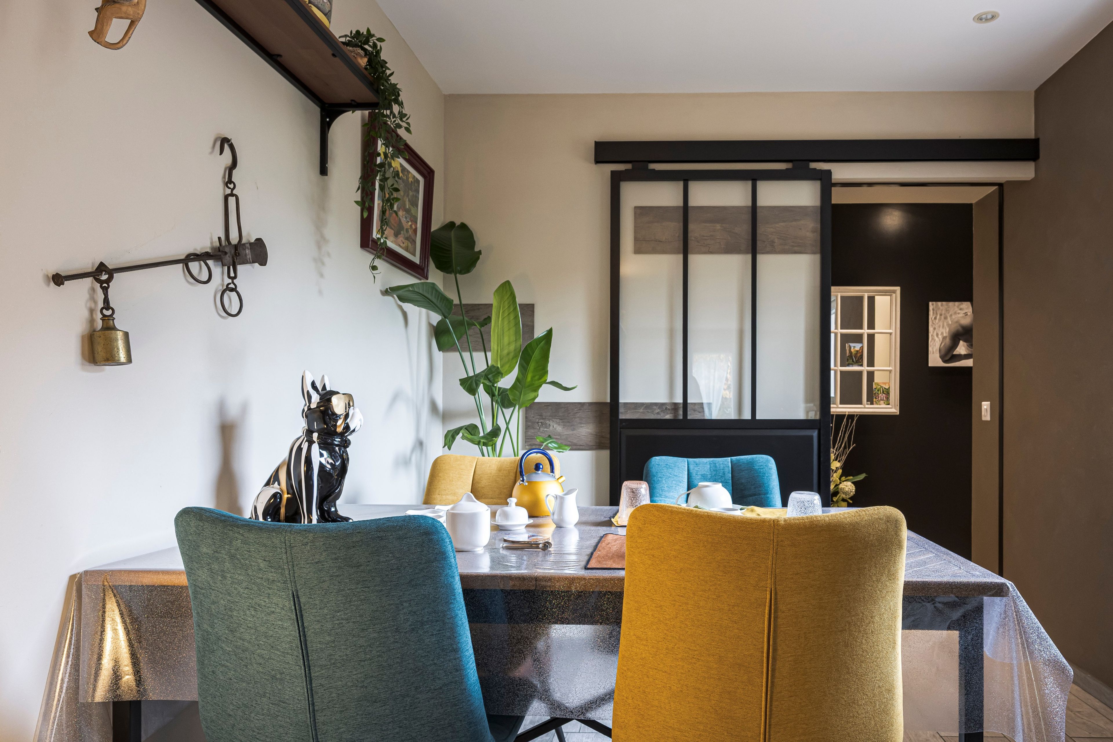 A dining area with a table set for two, chairs, a plant, and a wall-mounted hook.