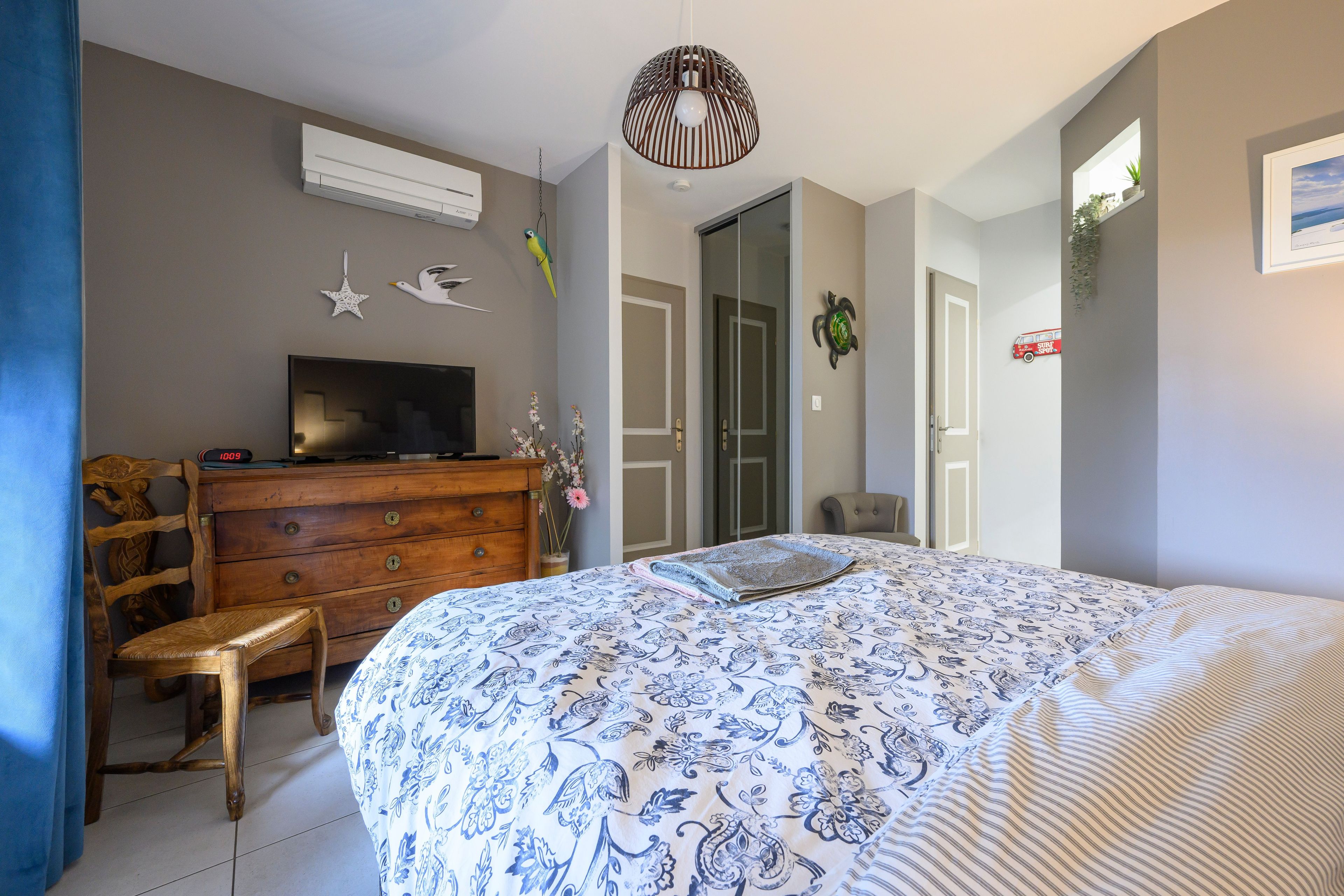A bedroom with a bed, dresser, television, and a wall-mounted air conditioner.