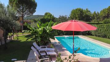 A swimming pool with lounge chairs and a red umbrella.