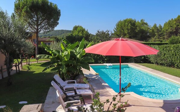 A swimming pool with lounge chairs and a red umbrella.