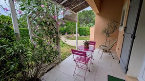 A covered patio area with a table and chairs, surrounded by greenery and a white trellis with pink flowers. - Bed and Breakfast 'Chambre - Le Clos Des Fontaines' with Private Pool, Wi-Fi and Air Conditioning (Pernes-les-Fontaines)