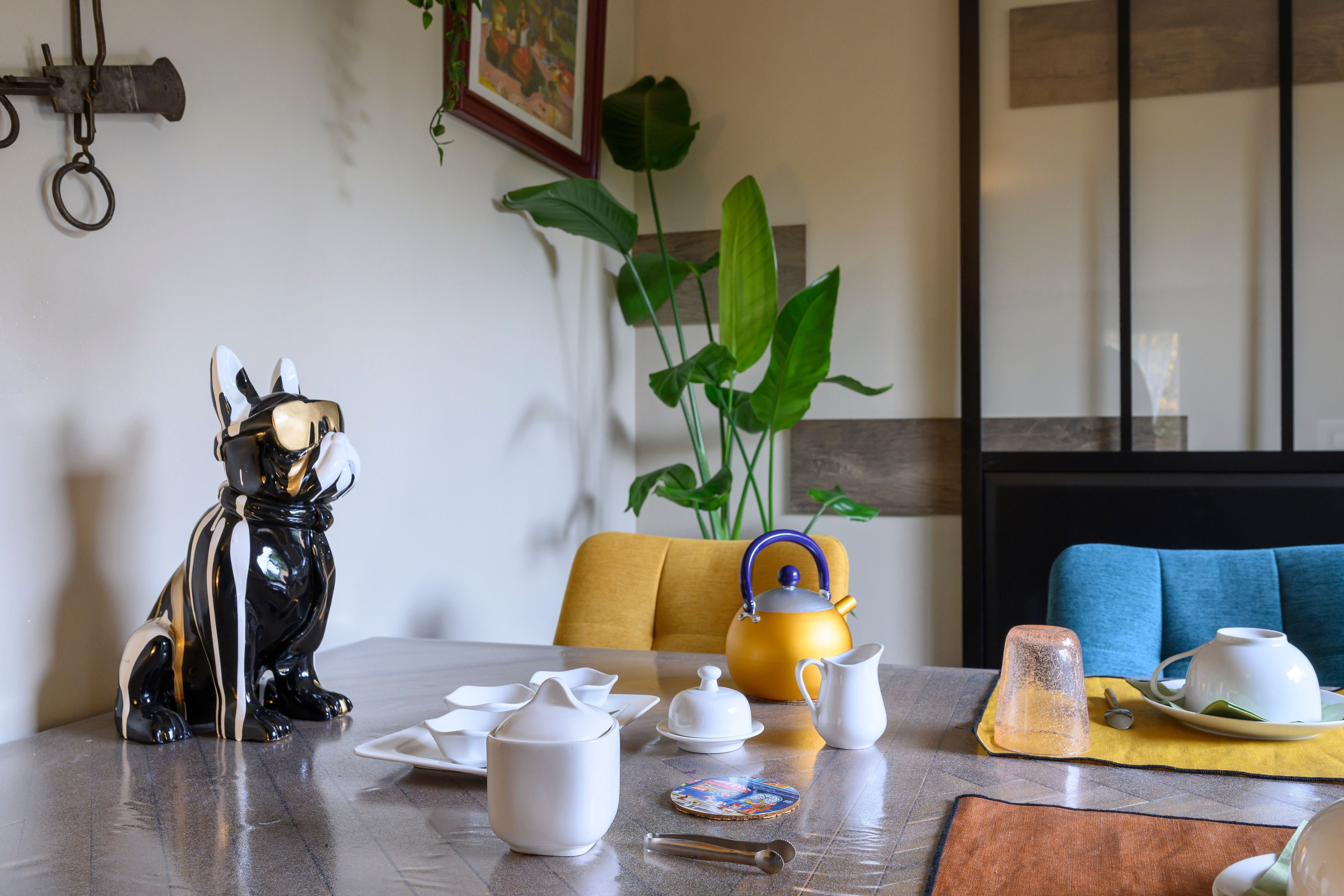 Een eettafel met een theepot, kopjes en een decoratief beeld.