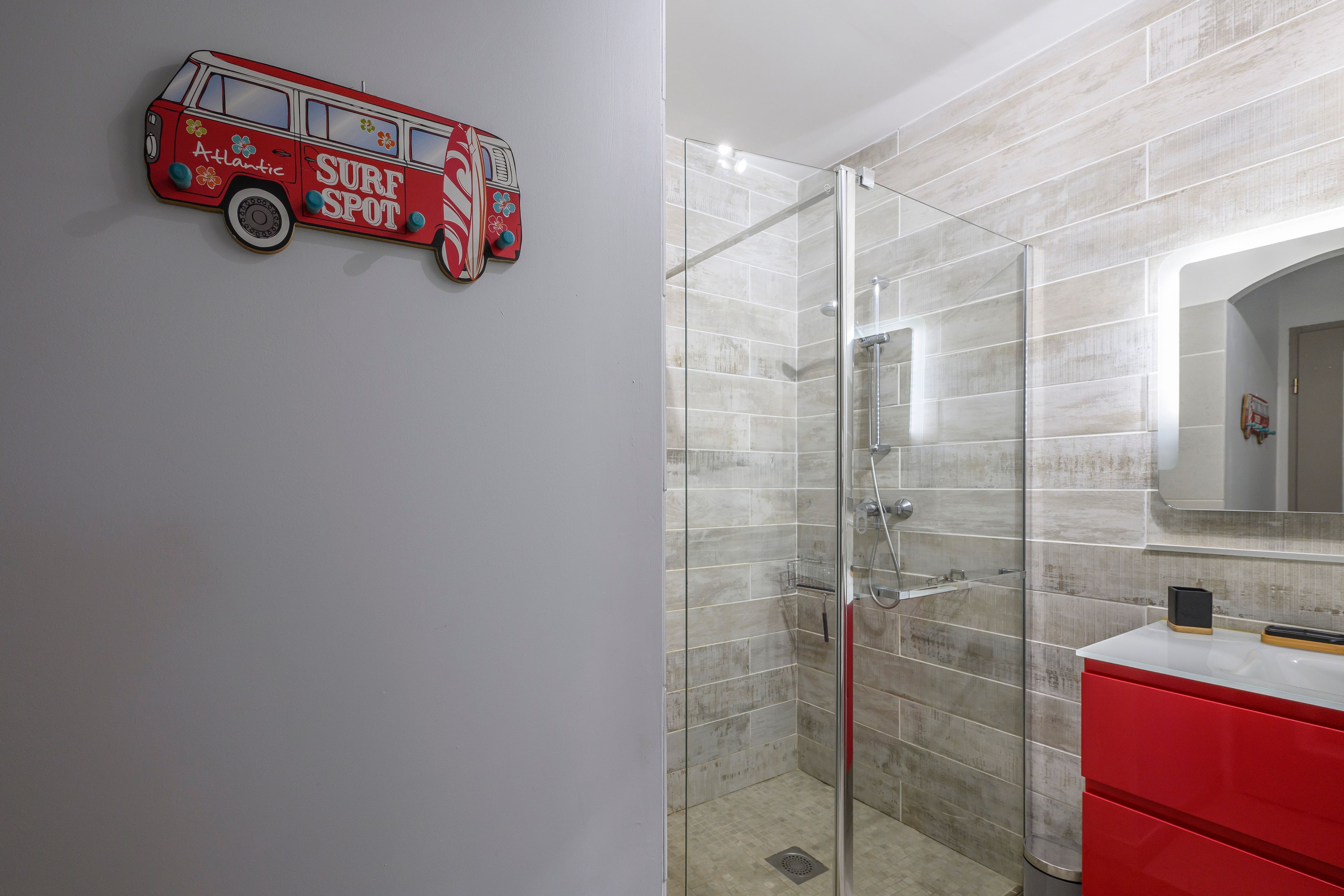 Une salle de bain avec une douche à parois de verre, un lavabo rouge et une décoration murale représentant un camion de pompiers.