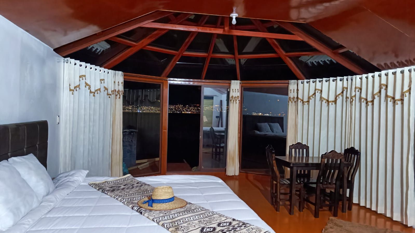 Un dormitorio con cama, una mesa de comedor con sillas y vistas a través de un ventanal.