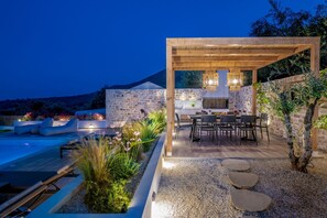 An outdoor kitchen area with a stone wall, a pergola, and a pool. - Villa Verde Zante in Kallithea (Zakynthos)