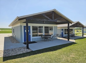 A modern building with a covered patio area, outdoor seating, and a view of a green field. - Cozy Arnolds Park Cottage with 6 Waterpark Daily Passes Included (Arnolds Park)