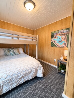 A room with a bunk bed, a small table with a lamp, and a painting of a water park on the wall. - Cozy Arnolds Park Cottage with 6 Waterpark Daily Passes Included (Arnolds Park)