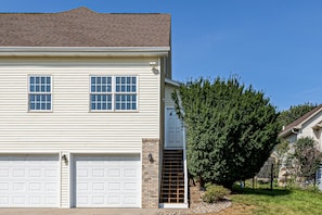A two-story house with a garage, a brick entryway, and a large evergreen tree in the front yard.