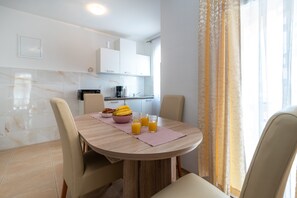 Una cocina moderna con armarios blancos, una mesa de comedor con sillas y una disposición para el desayuno con cruasanes y plátanos.