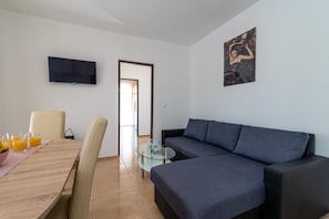 Una sala de estar moderna con un sofá, un televisor instalado en la pared y un comedor con mesa y sillas.