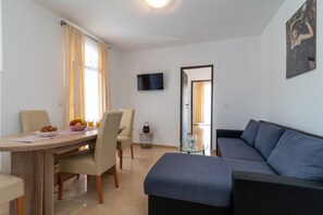 Een moderne woonkamer met een bank, een eettafel met stoelen en een aan de muur bevestigde televisie.