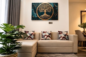 A living room with a beige sofa, a wall-mounted painting of a tree, and a potted plant. - Luxury Golf Retreat At Canterbury Lexus Golf Resort (Gonapola)