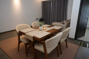 A dining area with a wooden table, beige chairs, and a small vase with a candle. - Luxury Golf Retreat At Canterbury Lexus Golf Resort (Gonapola)