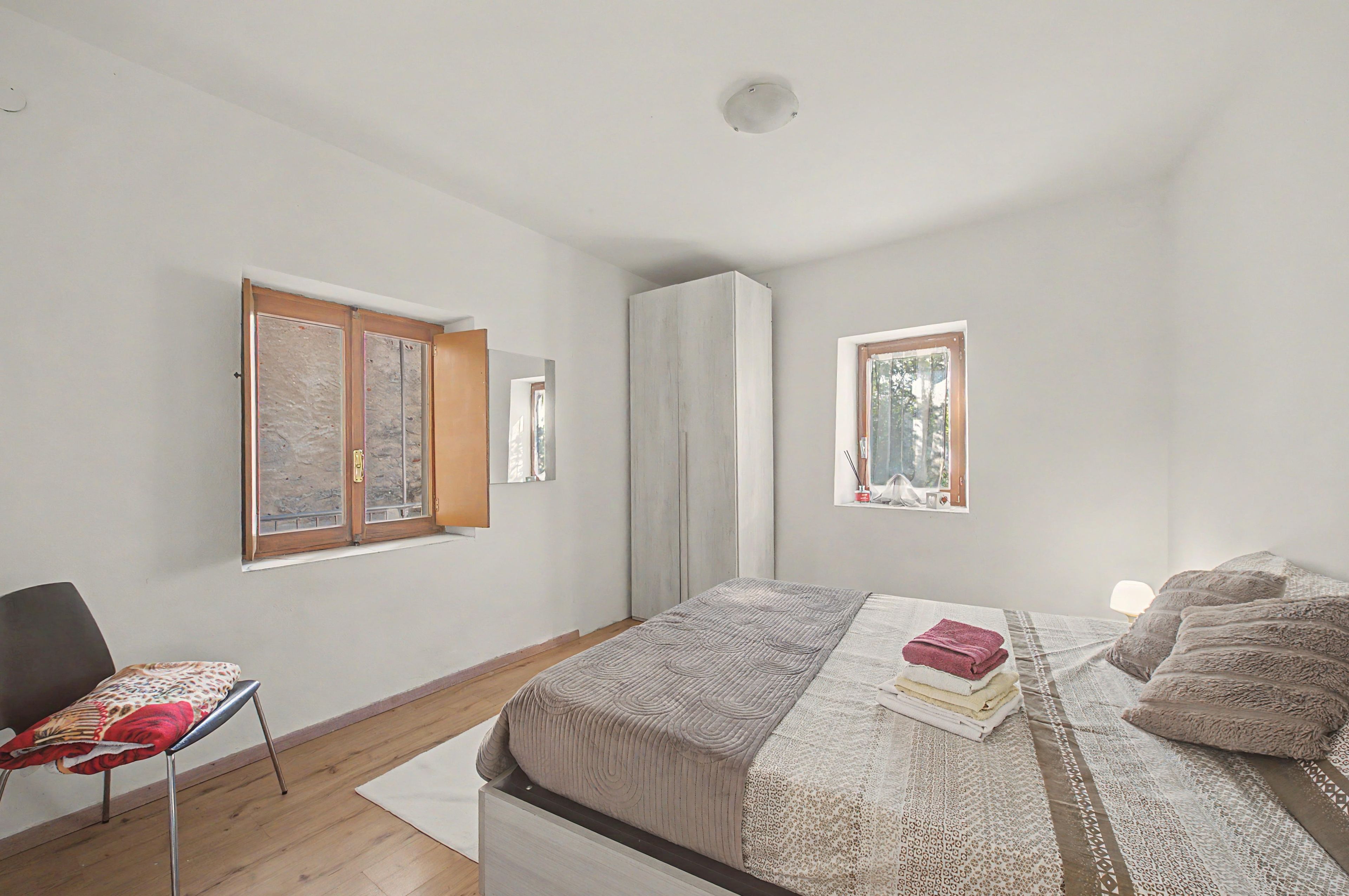 A bedroom with a bed, a chair, a window, and a wardrobe.