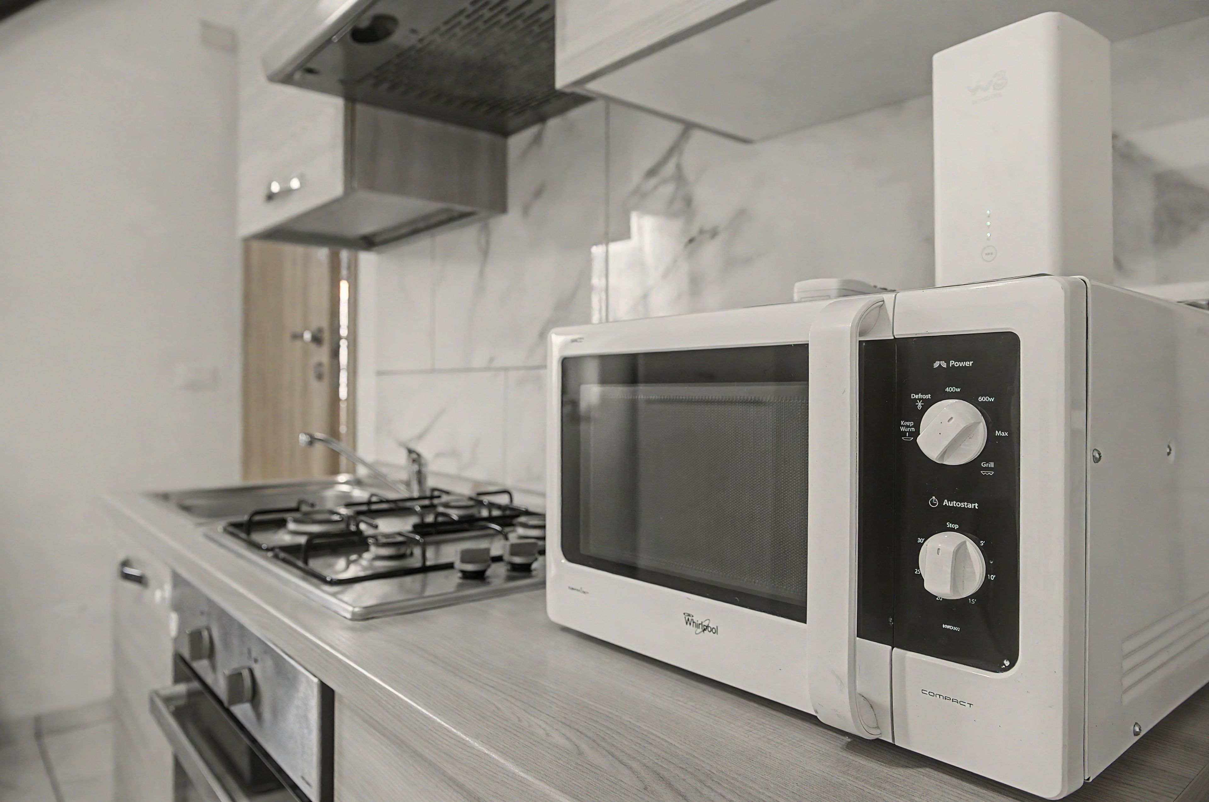 Micro-ondas compacto com visor digital e painel de controle, posicionado sobre uma bancada de cozinha.
