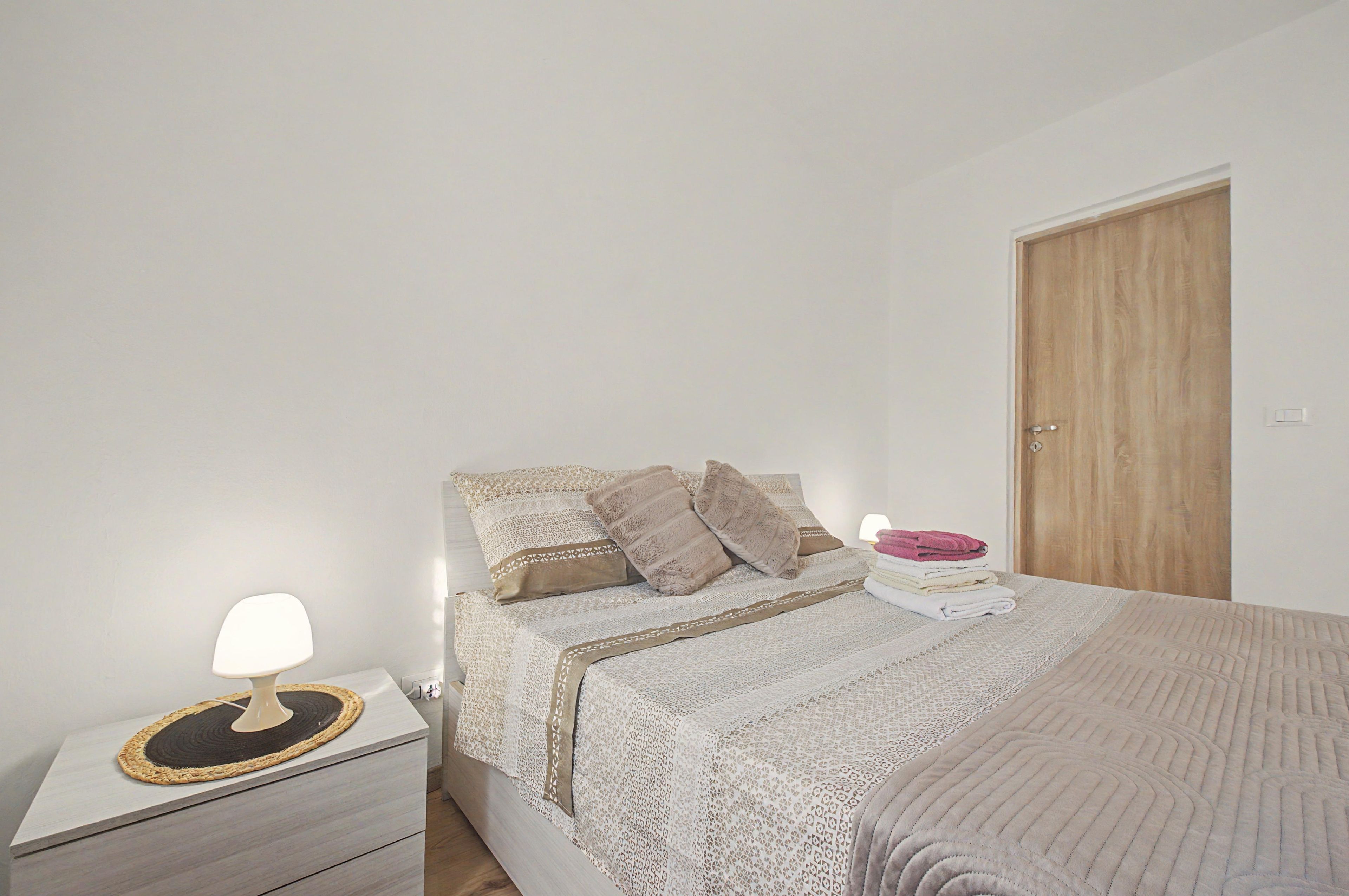 Quarto com cama, mesa de cabeceira e uma porta de madeira.
