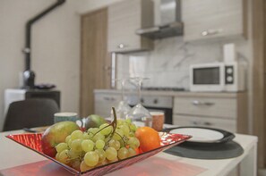 A dining table with a fruit bowl containing grapes, an orange, and a green apple. In the background, there is a kitchen area with a microwave and cabinets. - 'Nel Borghetto' Apartment with Shared Terrace, Balcony, and Wi-Fi (Ivrea)