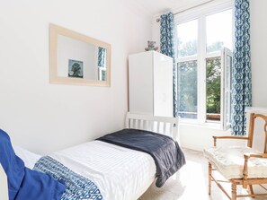 A bedroom with a bed, a chair, a wardrobe, a window with curtains, and a mirror on the wall. - Heritage Hideaway (Norwich)