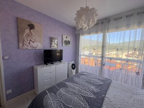 A bedroom with a bed, a television, a dresser, and a large window with a view of a red landscape. - 42-square-meter apartment, 1 bedroom, downtown, parking space (Aix-les-Bains)