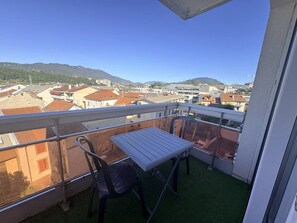 A balcony with a table and chairs, offering a view of a cityscape and mountains. - 42-square-meter apartment, 1 bedroom, downtown, parking (Aix-les-Bains)
