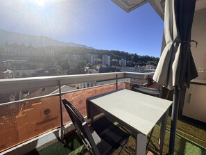 A balcony with a table and chairs, overlooking a cityscape with buildings and a mountain in the distance. - 42-square-meter apartment, 1 bedroom, downtown, parking space (Aix-les-Bains)