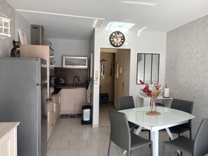 A modern kitchen with a refrigerator, stove, and microwave. There is a dining area with a table and chairs. - 42-square-meter apartment, 1 bedroom, downtown, parking (Aix-les-Bains)