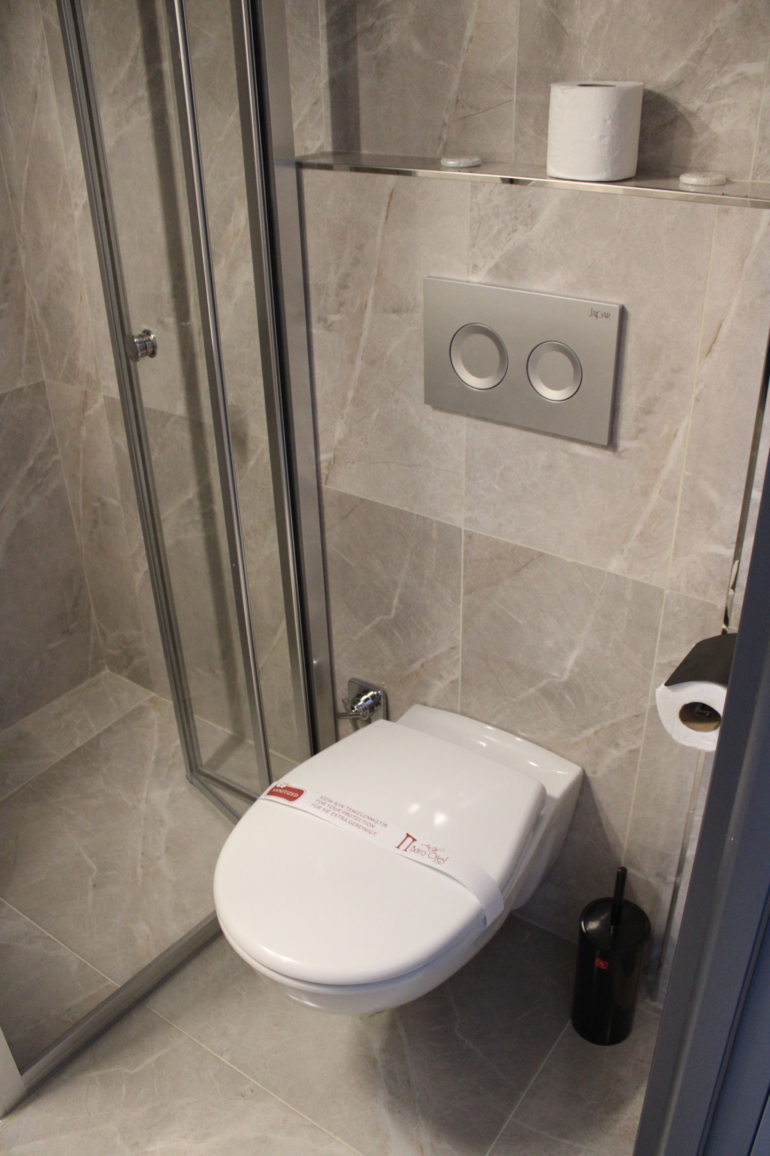 A modern bathroom with a glass shower enclosure, a toilet with a lid, and a paper towel dispenser.