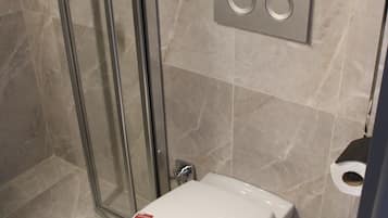 A modern bathroom with a glass shower enclosure, a toilet with a lid, and a paper towel dispenser.