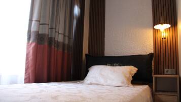 Quarto de hotel com cama, cortinas, luminária fixada na parede e mesa de cabeceira.