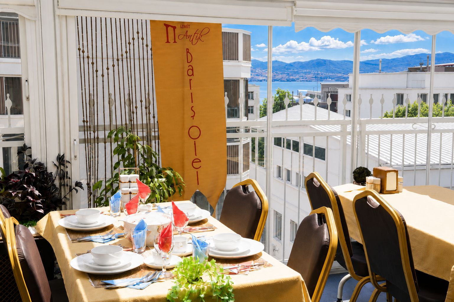 Zona pranzo con tavoli apparecchiati per un pasto, vista sulle montagne e uno striscione con il nome dell'hotel.