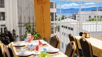 Zona pranzo con tavoli apparecchiati per un pasto, vista sulle montagne e uno striscione con il nome dell'hotel.