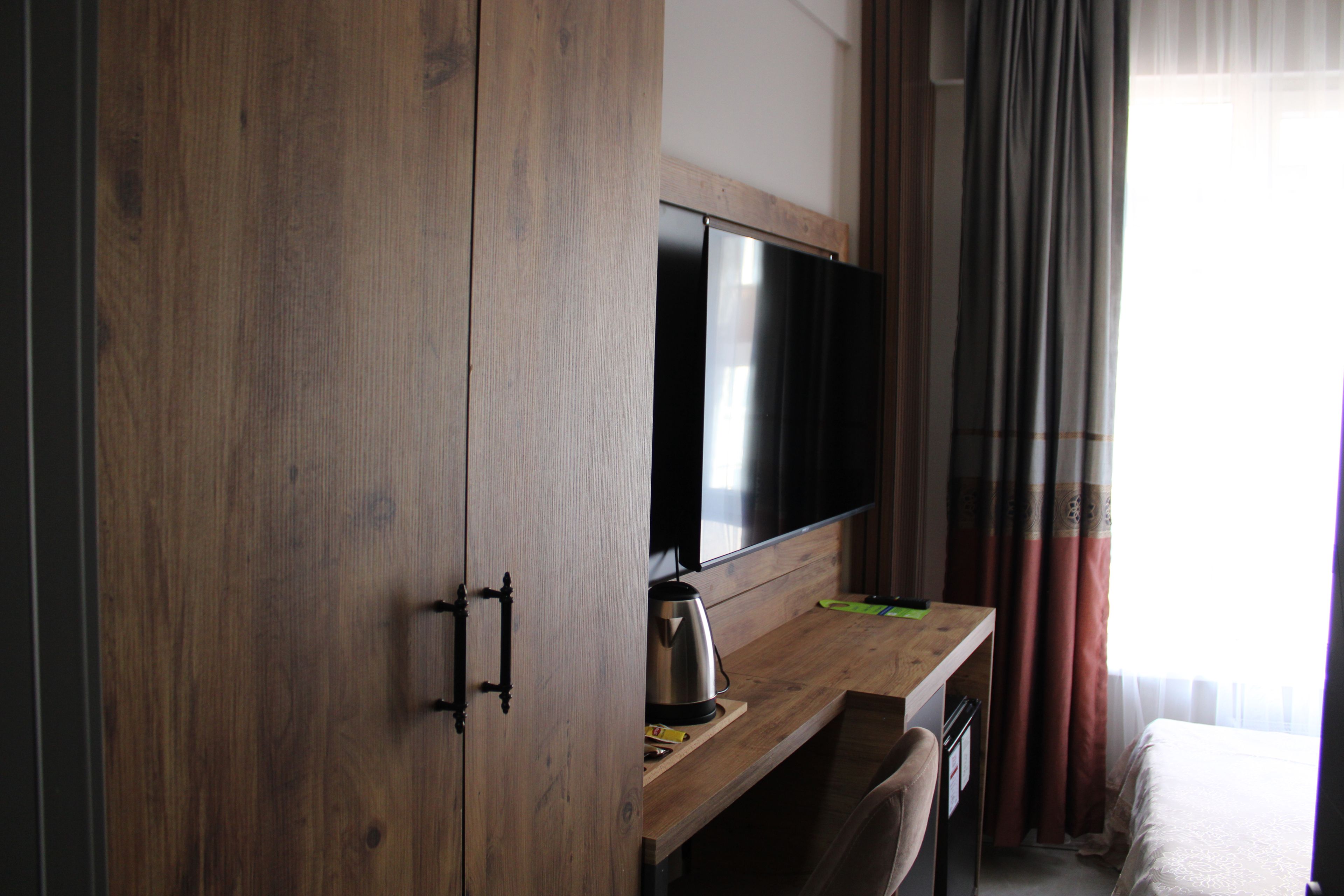 A hotel room with a wooden wardrobe, a flat-screen TV, a coffee maker, and a bed with a white bedspread.