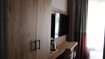 A hotel room with a wooden wardrobe, a flat-screen TV, a coffee maker, and a bed with a white bedspread.