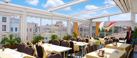 Un restaurant doté de nombreuses tables et chaises, de grandes fenêtres et offrant une vue sur les bâtiments qui se dressent à l'arrière-plan.