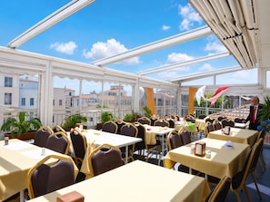 A restaurant with multiple tables and chairs, large windows, and a view of buildings in the background.