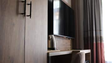 Una habitación con un armario de madera, un escritorio con una silla, un televisor de pantalla plana y una ventana con cortinas.