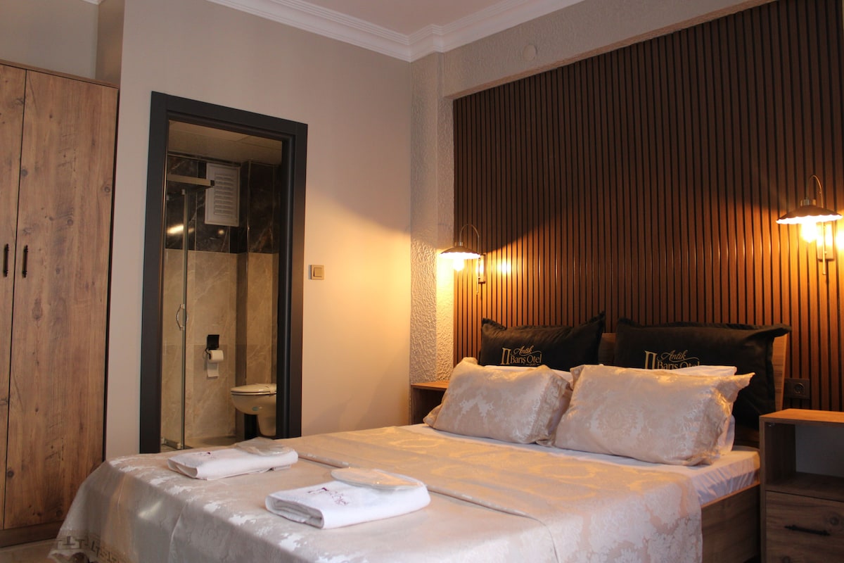 Une chambre d’hôtel comprenant un lit, une armoire en bois, une salle de bain avec des toilettes et deux lampes fixées au mur.