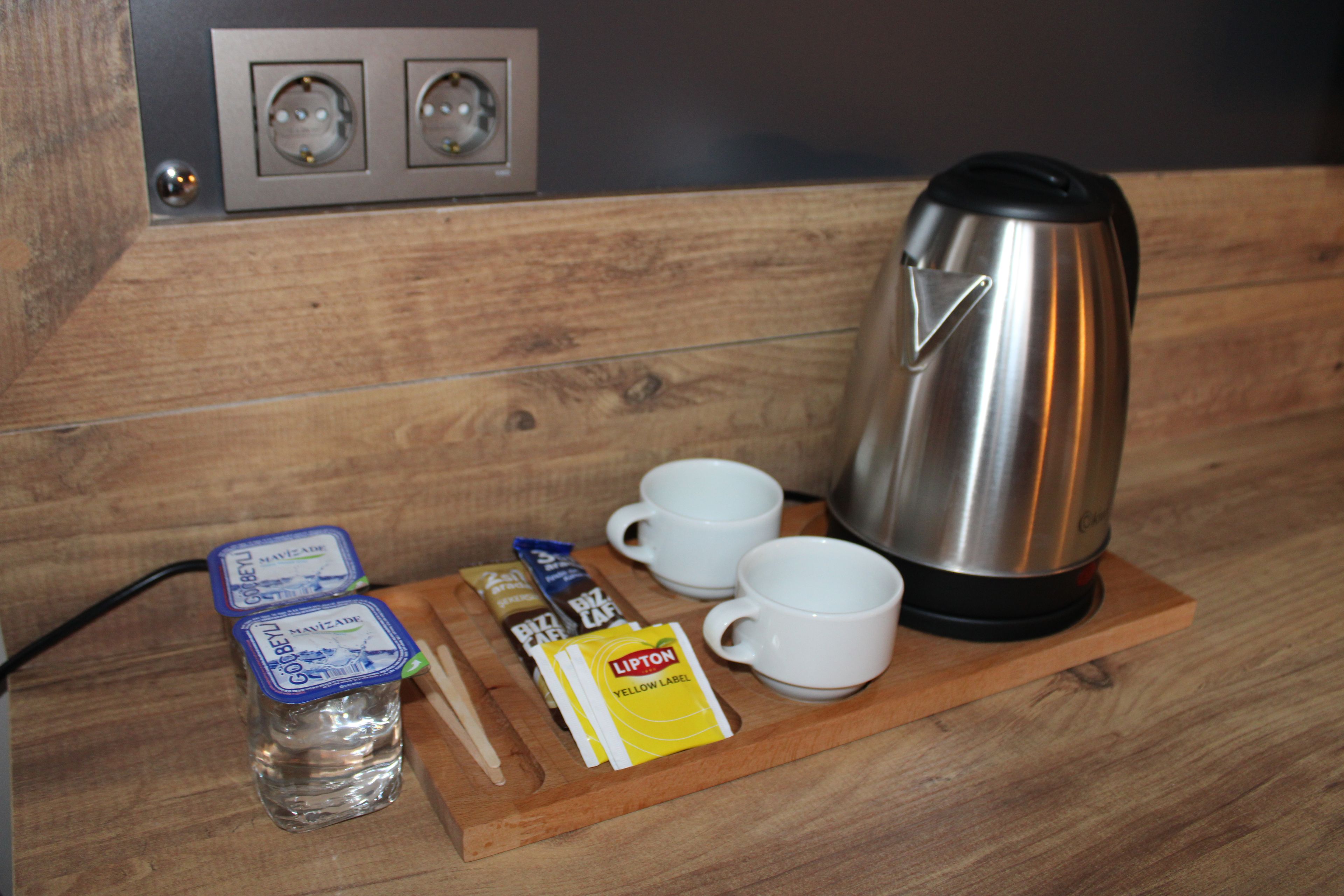 A wooden table with a kettle, two white cups, a bottle of water, and some packaged food items.