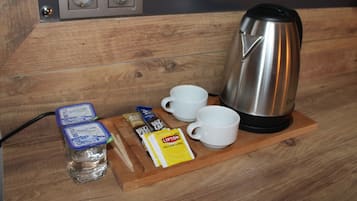 A wooden table with a kettle, two white cups, a bottle of water, and some packaged food items.