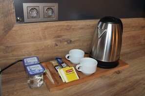 A wooden table with a kettle, two white cups, a bottle of water, and some packaged food items. - Antik Barış Otel (Izmit)